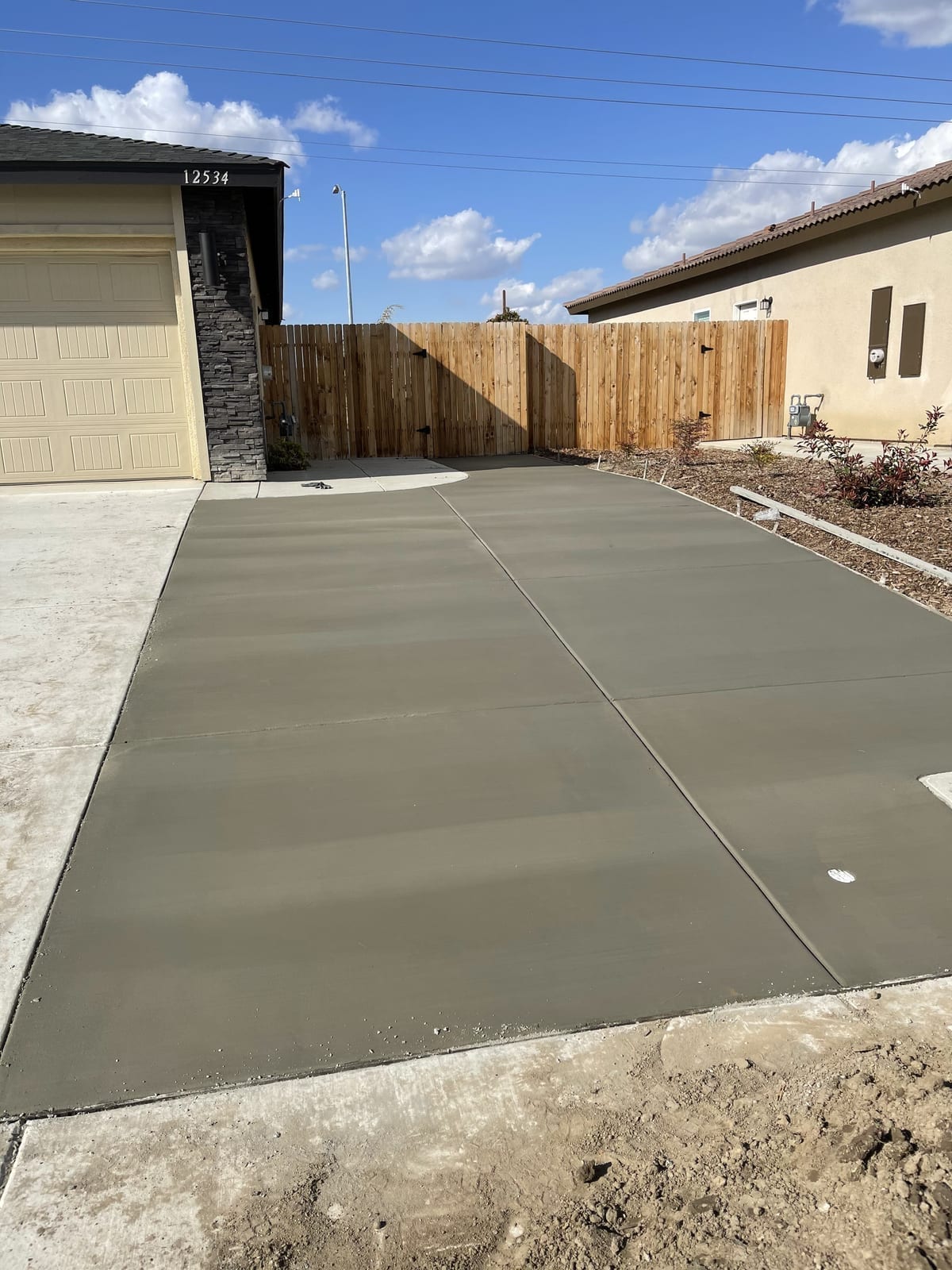 Modern home concrete driveway with broom finish, freshly poured with crisp control joints and a wood fence backdrop