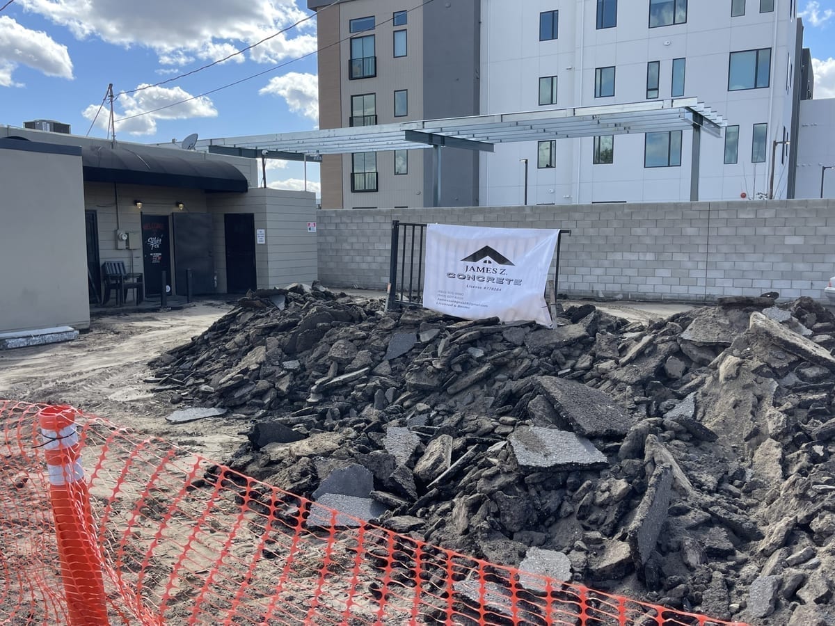James Z. Concrete branded sign on a commercial demolition site with rubble piled up and orange safety fencing