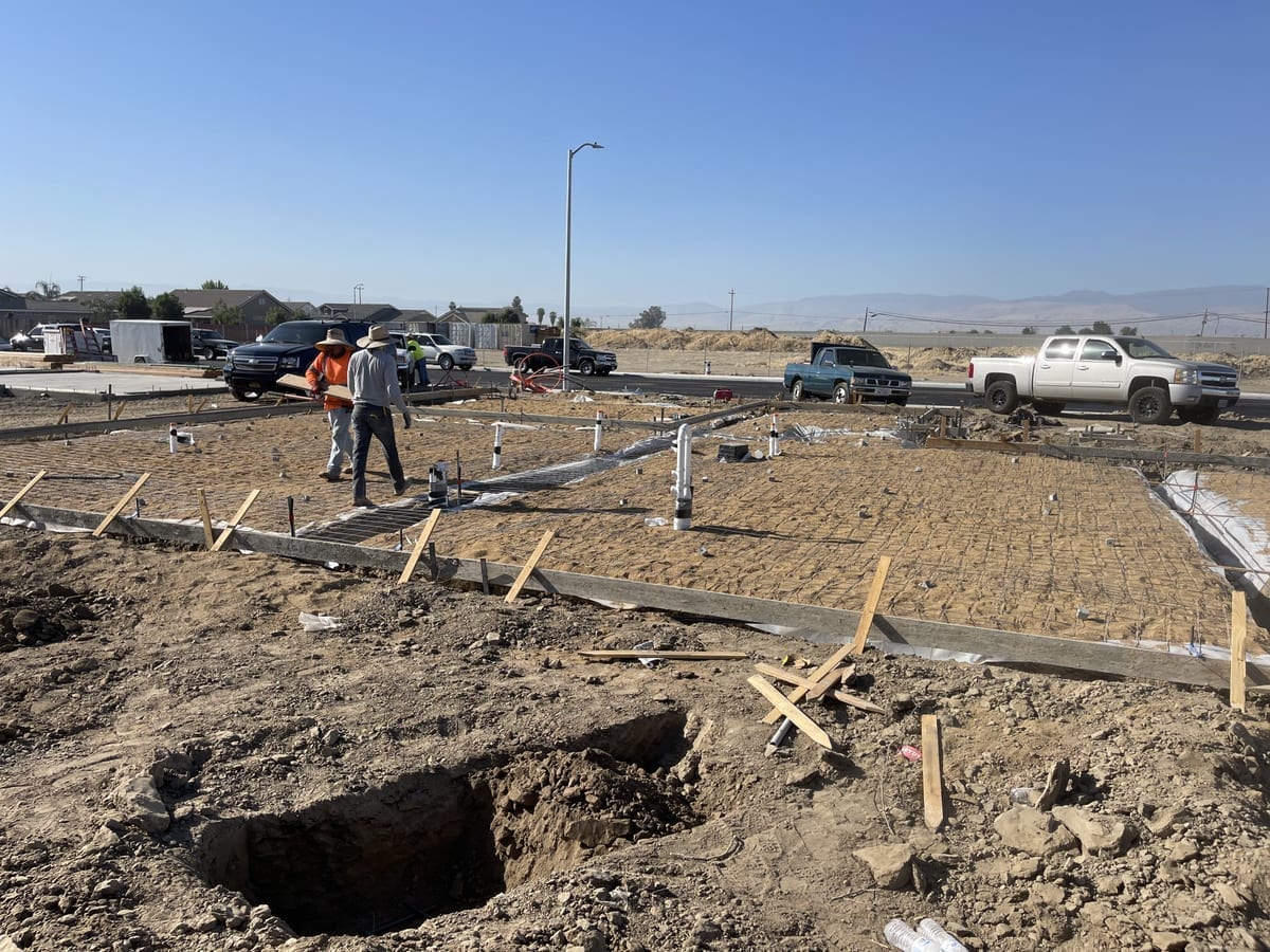 James Z. Concrete crew assessing a foundation site with forms staked out and trucks staged on a residential lot